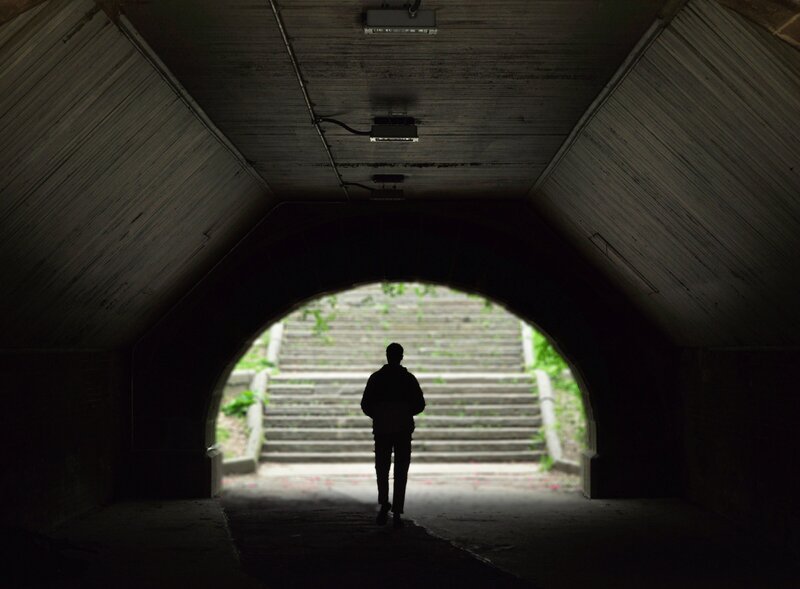 Man walking through a dark tunnel with light at the end