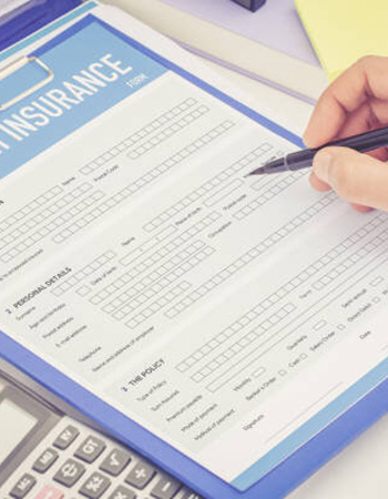 A person's hand is shown filling out health insurance paperwork
