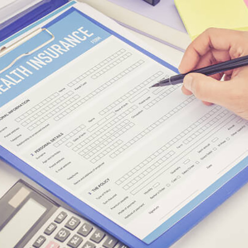 A hand is shown filling out a medical insurance form in pen.