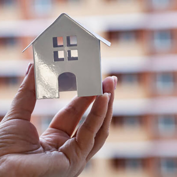 House in hand on the background of a building under construction. Buying a property.